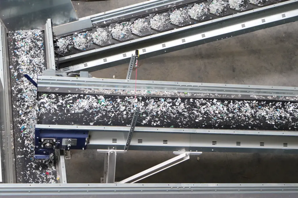 輸送帶上載有經由 SPALECK 篩分機按尺寸篩分過的塑膠廢料，這些廢料將送往近紅外線（NIR）分選設備進行進一步分選。