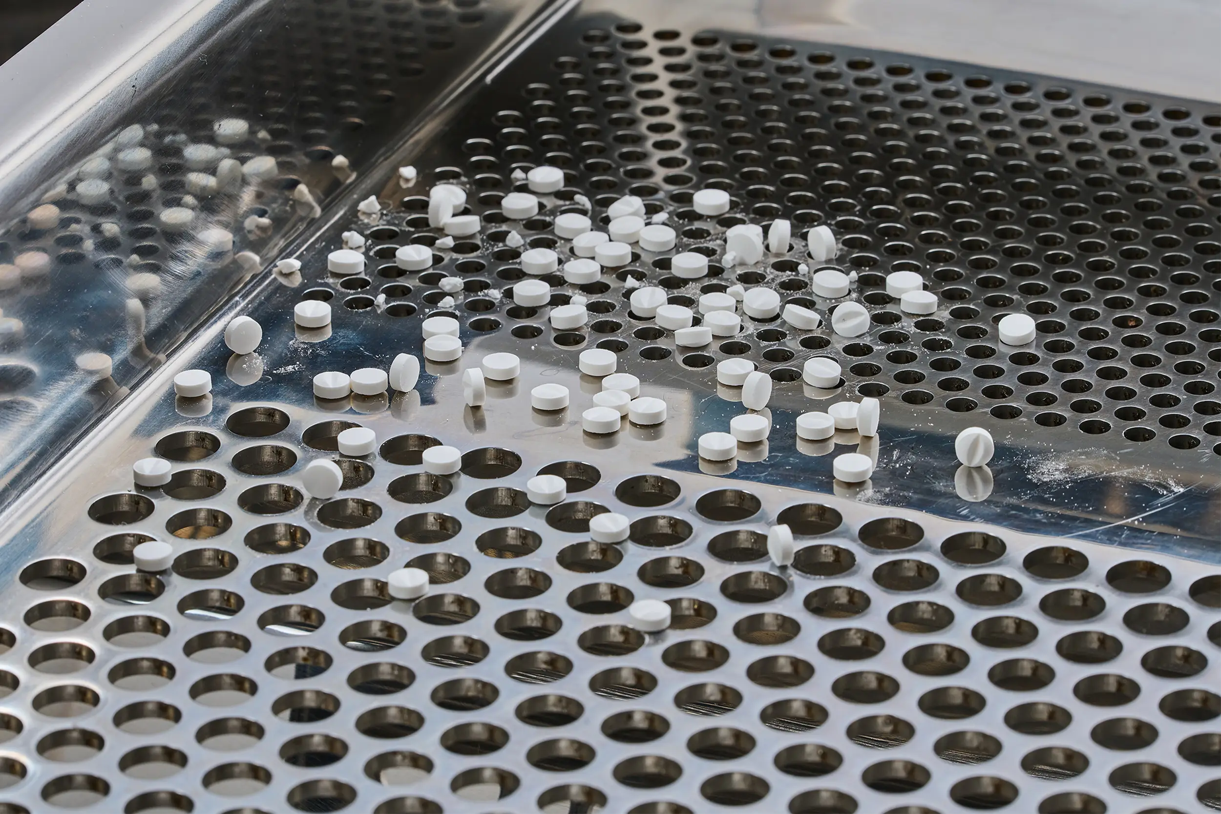 製藥篩分機中，金屬篩網上的白色藥錠。