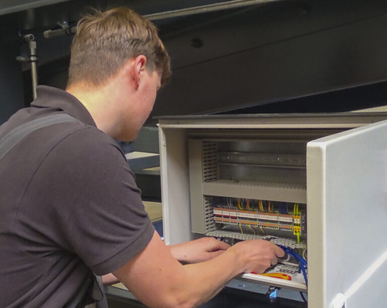 A mechatronics technician apprentice is working on the control cabinet