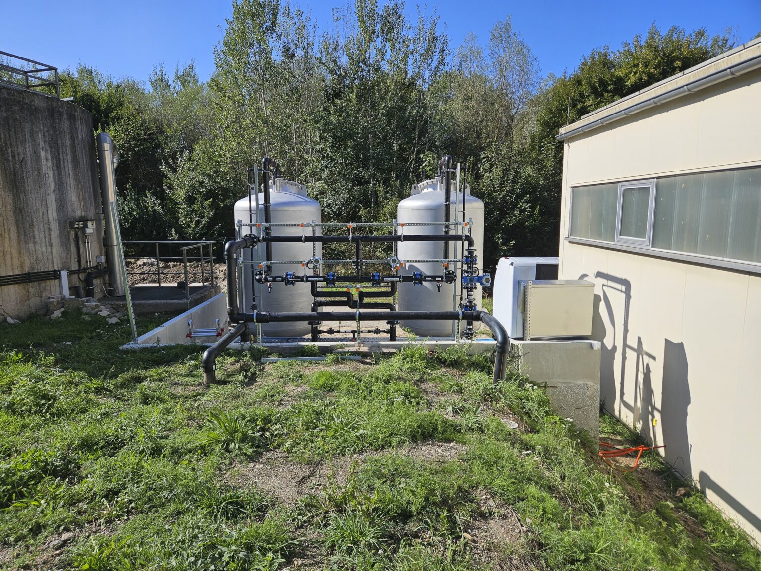 Zwei Tanks zur Aktivkohlefiltration mit zugehöriger Verrohrung neben einer Werkshalle.