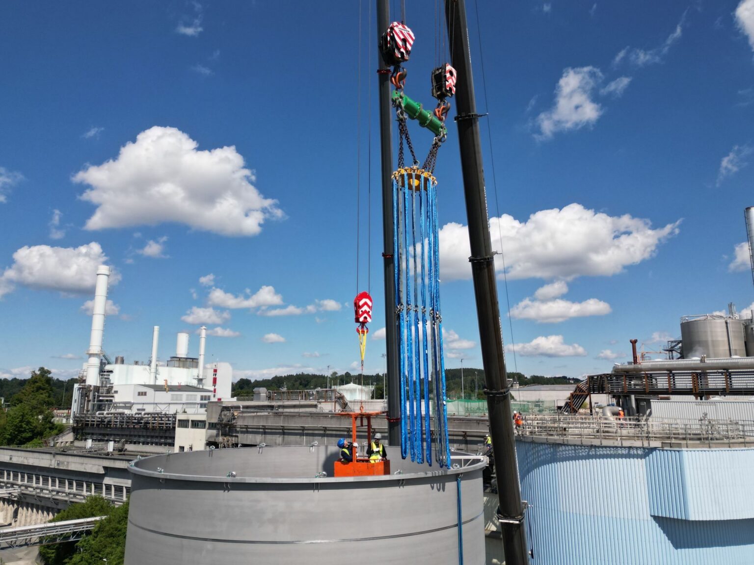 Installation eines großen Tanks für die Wasseraufbereitung in der Industrie mit einem Kran. Handwerker arbeiten im Tank